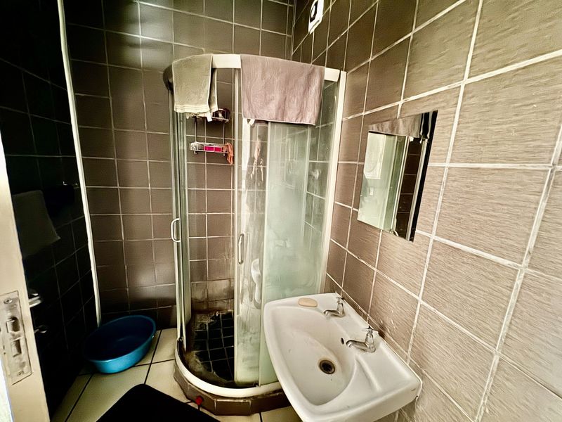 A compact bathroom featuring a corner shower cubicle, wall-mounted basin, and full-height wall tiling.