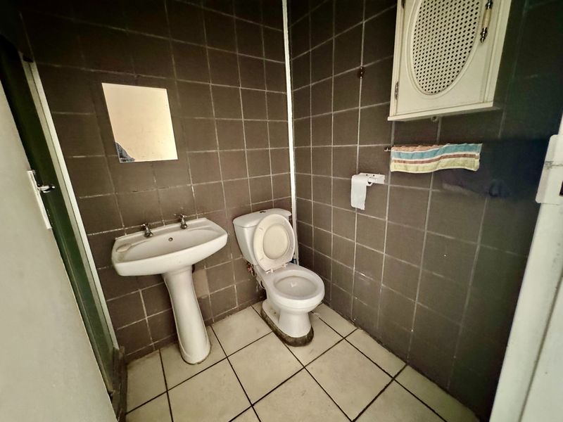 A dated bathroom featuring dark wall tiles, a pedestal basin, and a standard toilet, requiring cosmetic updates to improve its overall condition and appeal.