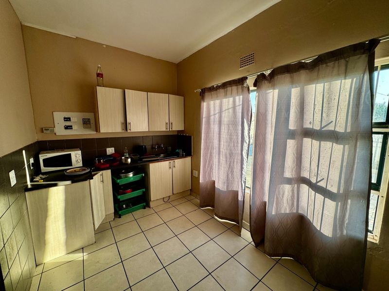 A functional kitchen featuring built-in cabinetry, tiled flooring, and a tiled backsplash, with direct access to an outdoor area through a security gate.