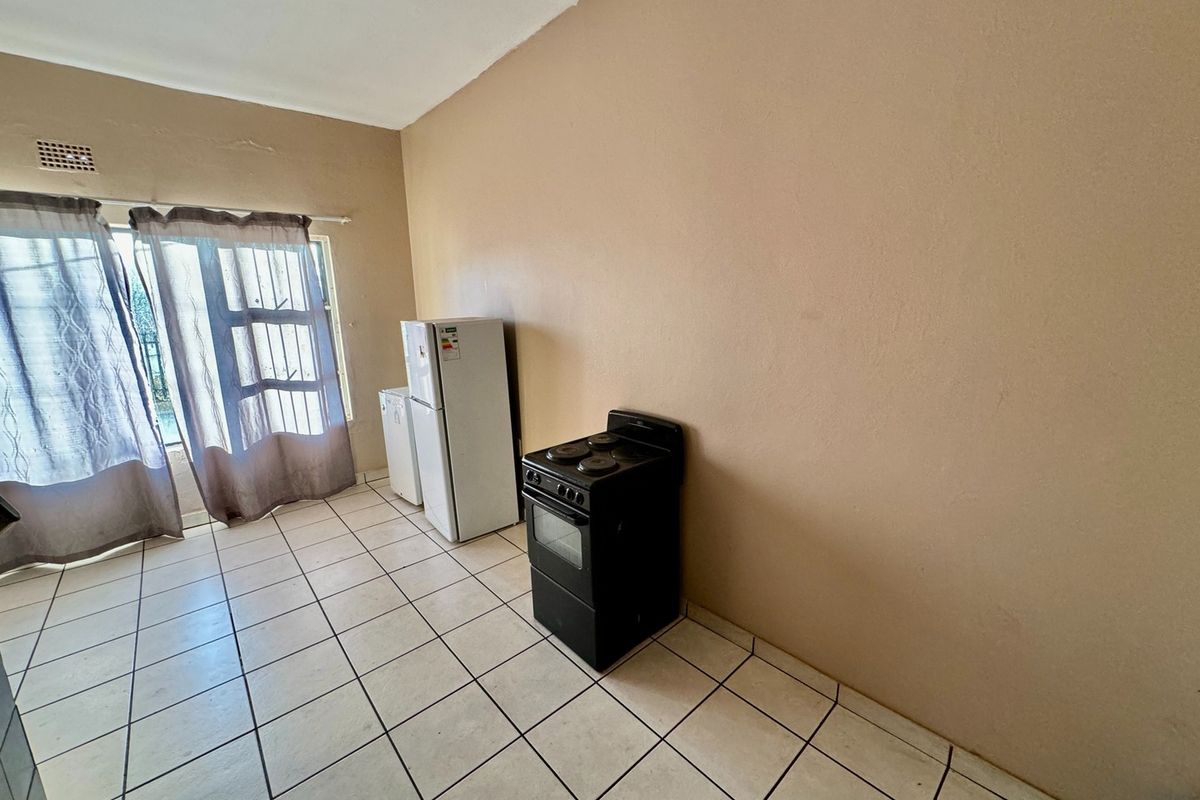 A basic kitchen area featuring ceramic floor tiles and a sliding door leading to the exterior, currently presented as an empty, functional space.