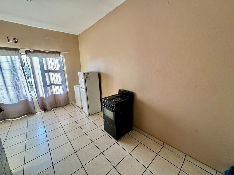 A basic kitchen area featuring ceramic floor tiles and a sliding door leading to the exterior, currently presented as an empty, functional space.
