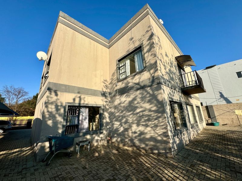 Rear exterior view of the apartment building featuring a paved courtyard, balcony with metal railing, and security bars on ground floor windows.