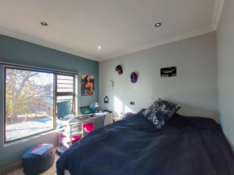 A functional bedroom featuring tiled flooring, recessed downlighting, and a large window providing natural light and exterior views.