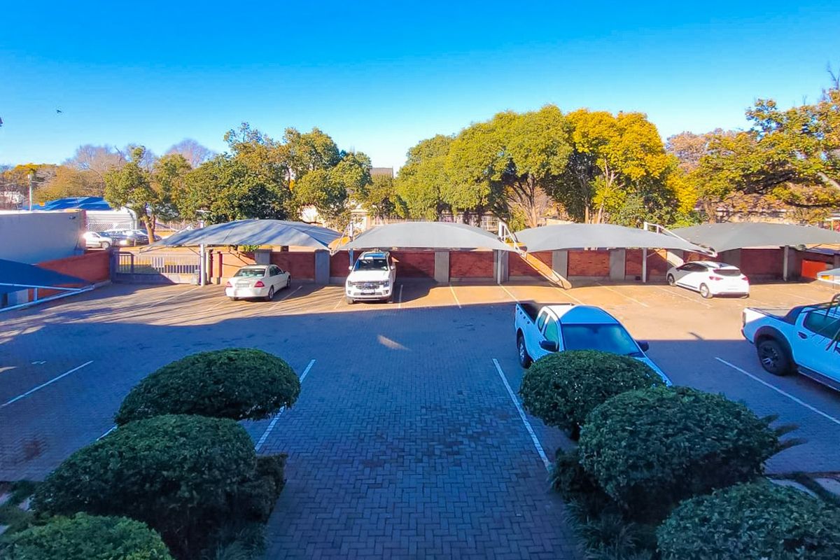 An outdoor parking area featuring paved surfaces, covered carport bays, and established perimeter landscaping within a residential apartment complex.