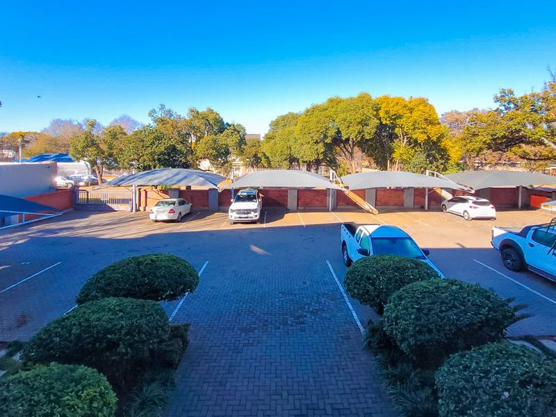 An outdoor parking area featuring paved surfaces, covered carport bays, and established perimeter landscaping within a residential apartment complex.