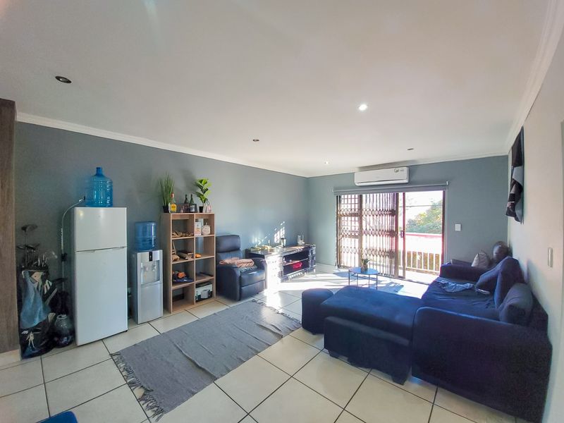 Spacious living room featuring tiled flooring, recessed lighting, and a split-system air conditioner, with direct access to an outdoor balcony through a sliding glass door.