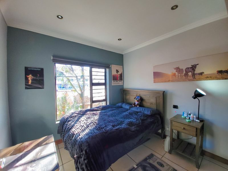 A well-lit bedroom featuring tiled flooring, recessed downlighting, and a large window with a roller blind.