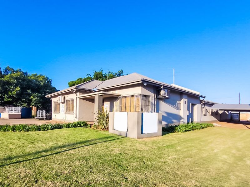 A well-maintained commercial property featuring a landscaped lawn, paved driveway, secure window bars, and an attached carport.