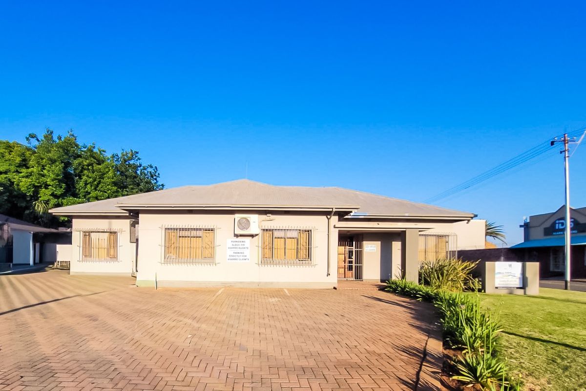 Front exterior view of a commercial property featuring a paved driveway, security bars on windows, and a well-maintained garden area.