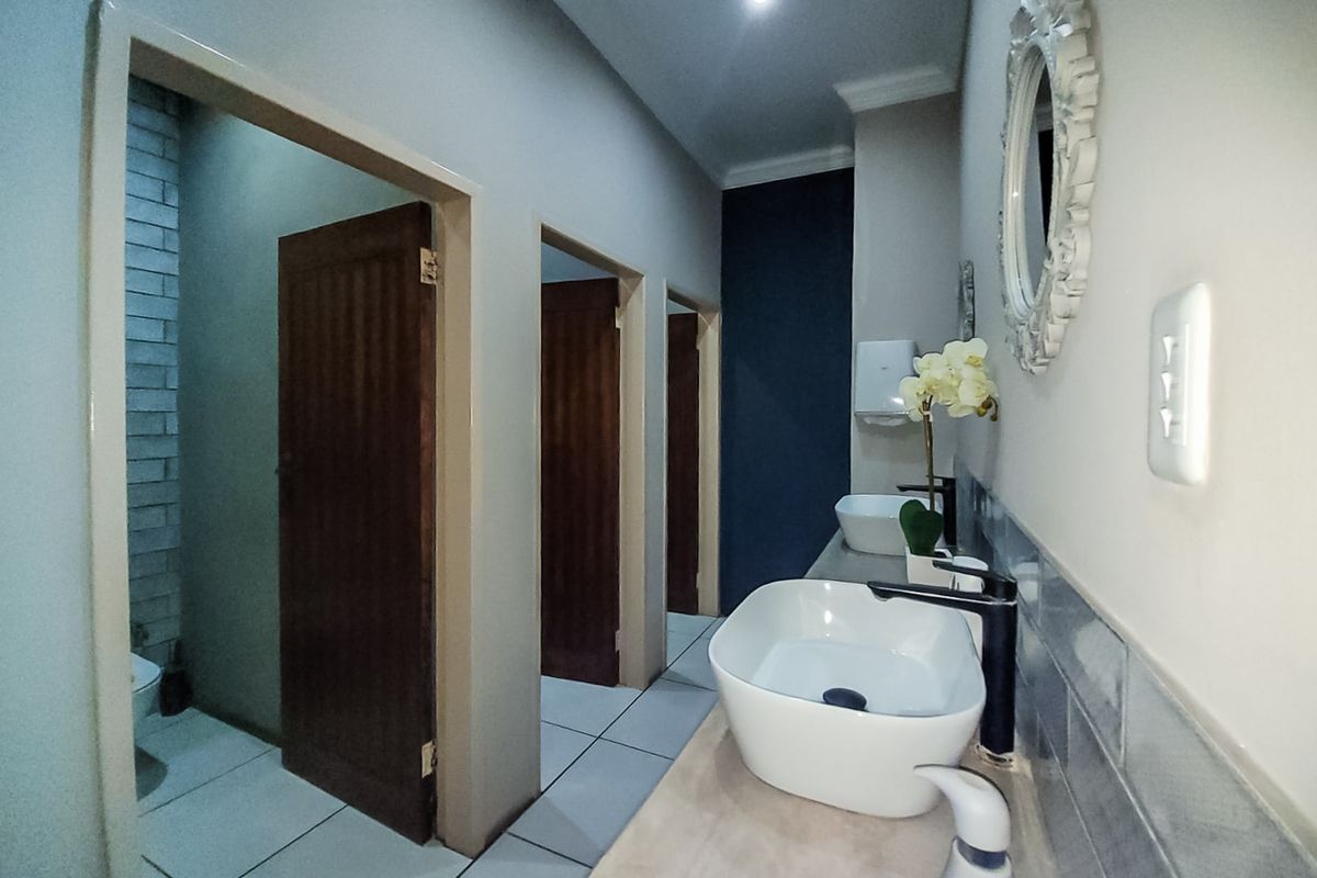 A modern commercial bathroom featuring dual vessel sinks, contemporary black faucets, tiled backsplash, and multiple private stalls with wooden doors.