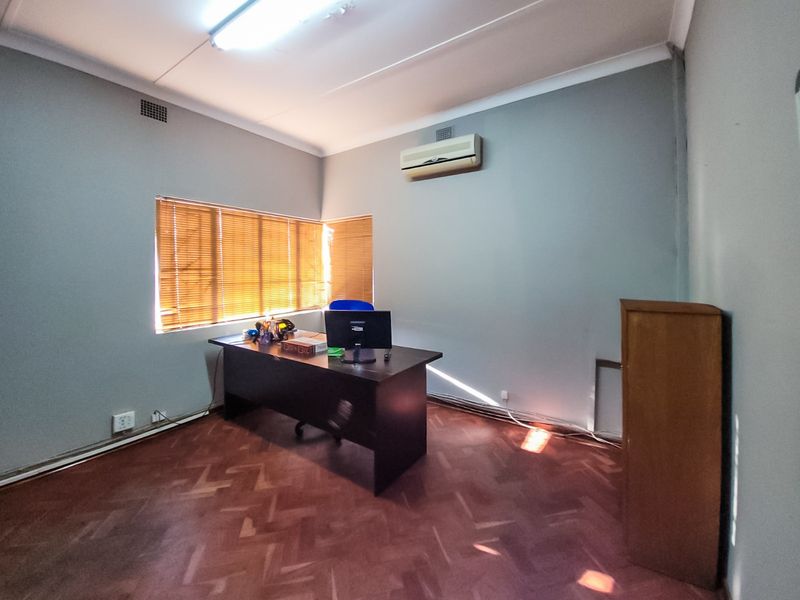 A functional office space featuring parquet flooring, an installed air conditioning unit, and venetian blinds, providing a practical environment for commercial use.