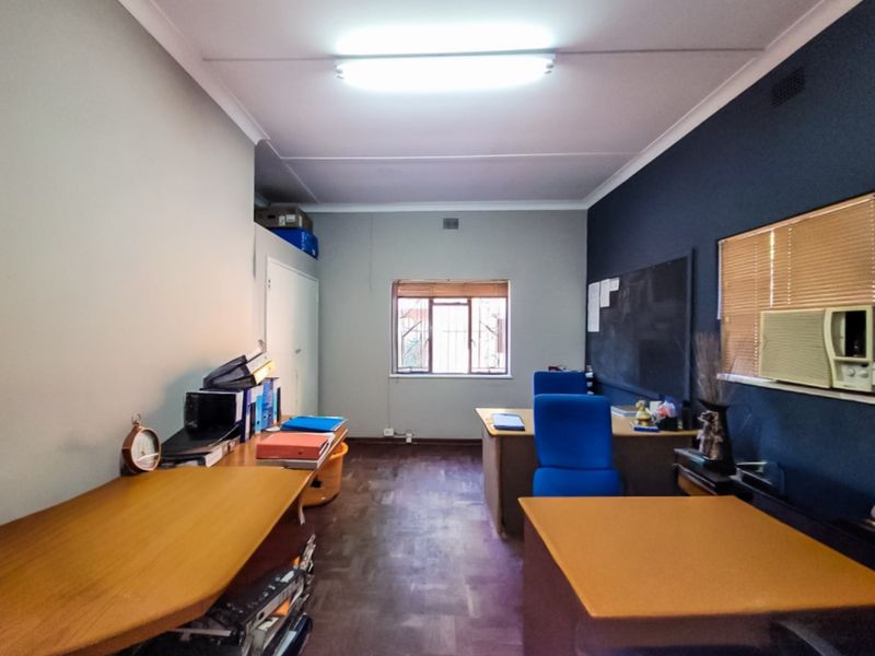 A functional office space featuring parquet flooring, a window with security bars, built-in storage, and an integrated air conditioning unit.