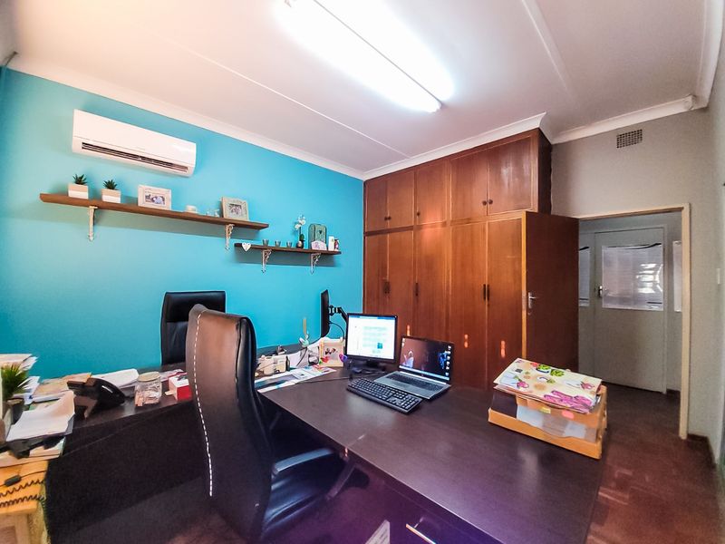A functional office space featuring built-in wooden cabinetry, floating wall shelves, and a wall-mounted air conditioning unit.