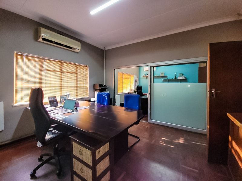 A functional commercial office space featuring a sliding glass partition, venetian blinds, and a wall-mounted air conditioning unit.