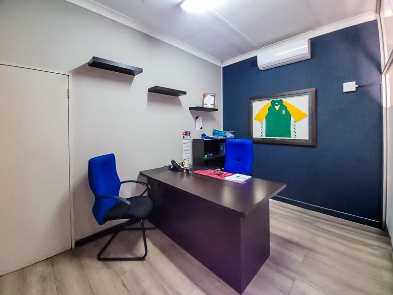 A functional commercial office space featuring laminate flooring, a wall-mounted split-system air conditioner, and decorative floating shelves.