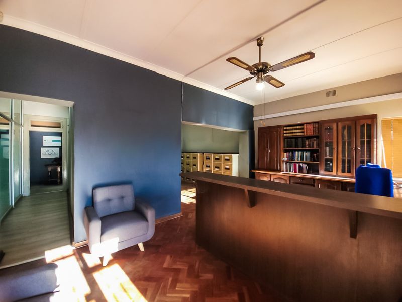 A professional office space featuring a reception counter, built-in wooden cabinetry, a ceiling fan, and classic parquet flooring.