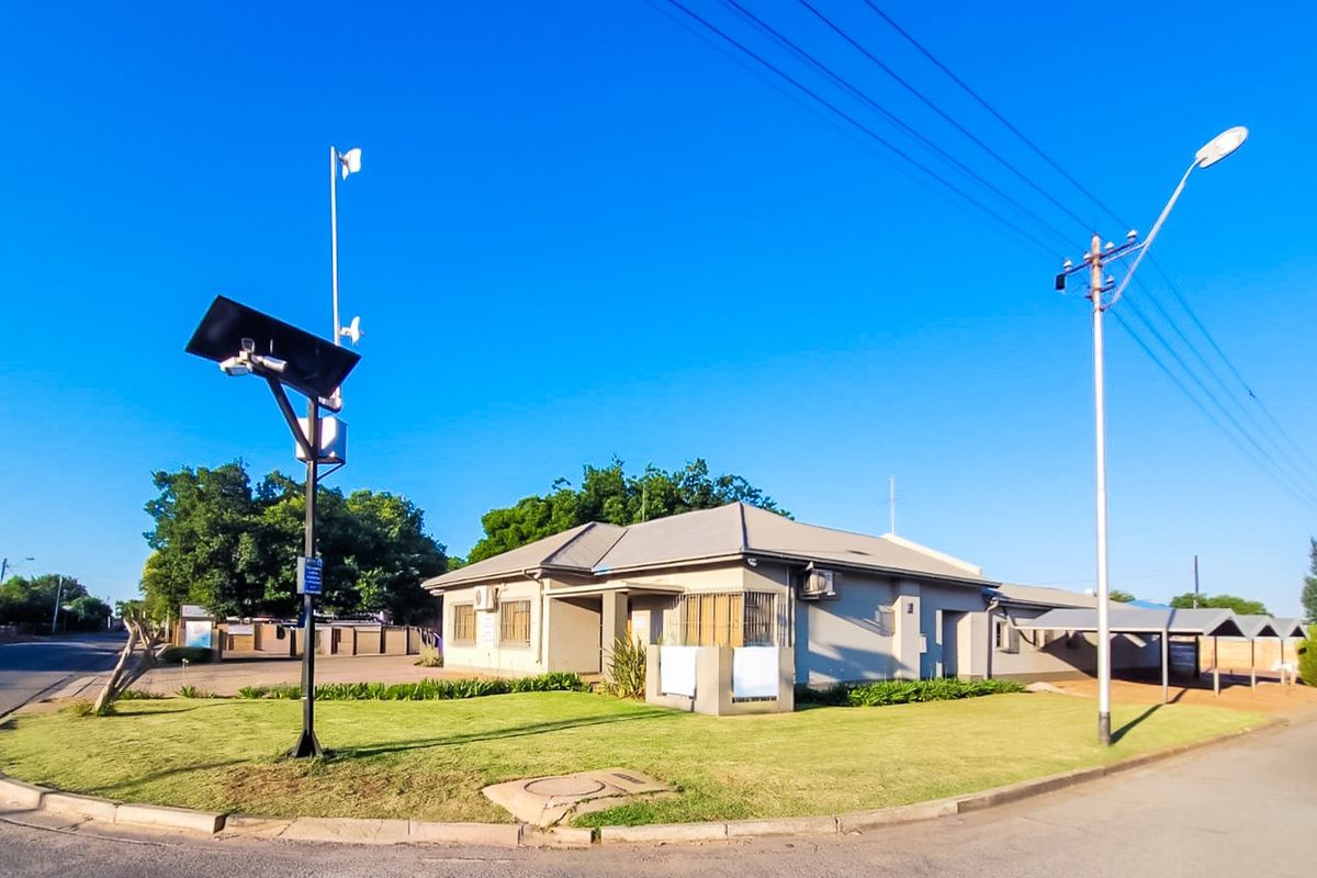 Corner commercial property featuring a well-maintained lawn, solar-powered security infrastructure, and covered parking facilities.
