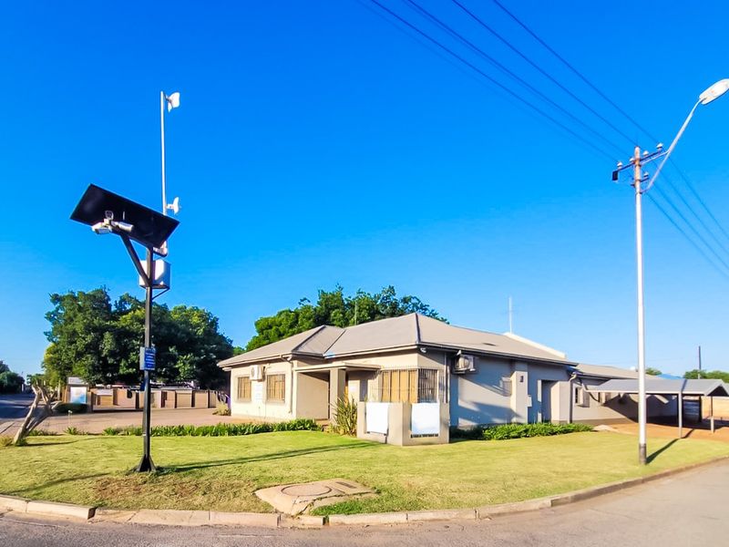 Corner commercial property featuring a well-maintained lawn, solar-powered security infrastructure, and covered parking facilities.