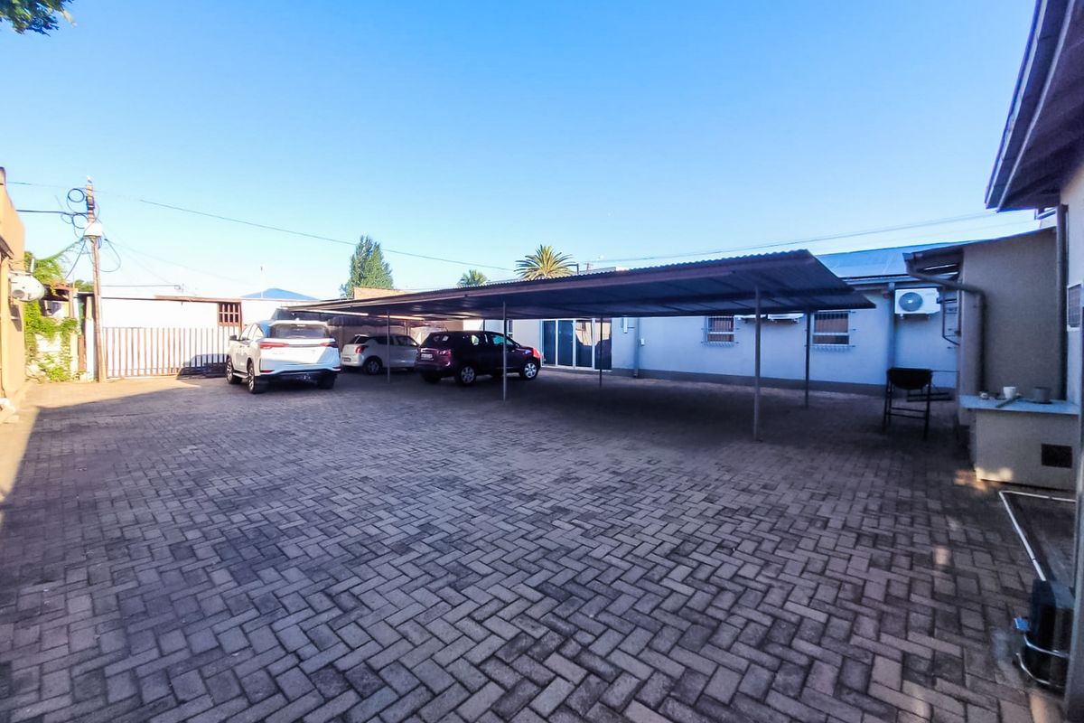 A spacious paved rear courtyard featuring a large covered carport area, providing ample parking space for multiple vehicles.