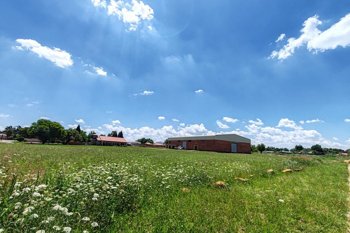 A wide-angle view of an industrial warehouse property featuring a brick exterior and large roller shutter doors, set within a spacious open field.