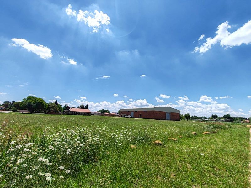 A wide-angle view of an industrial warehouse property featuring a brick exterior and large roller shutter doors, set within a spacious open field.