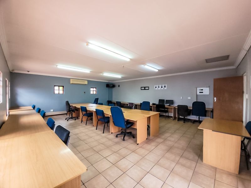 A spacious commercial office area featuring ceramic tiled flooring, fluorescent lighting, and a wall-mounted air conditioning unit.