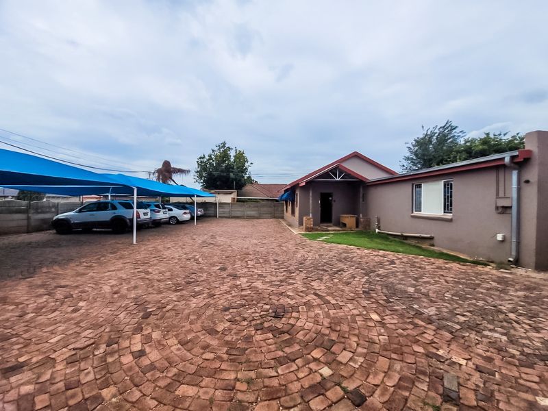 Commercial property exterior featuring a large brick-paved parking area with a shade cloth carport and secure boundary walling.