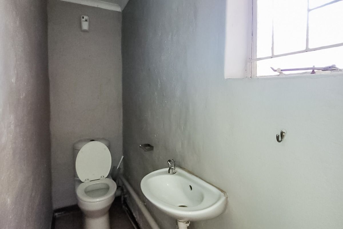 A compact, functional bathroom featuring a wall-mounted basin, toilet, and tiled flooring, requiring cosmetic updates to improve its overall condition and appeal.