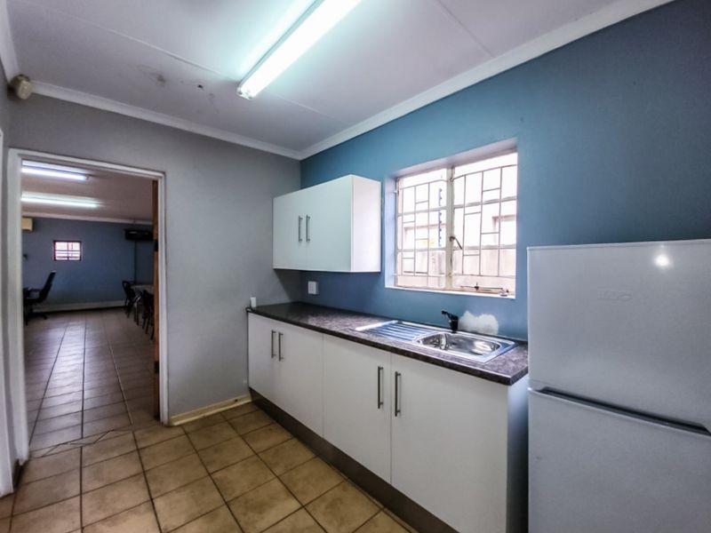 A functional kitchenette featuring white cabinetry, a stainless steel sink, and a window with security bars, providing a practical utility space.
