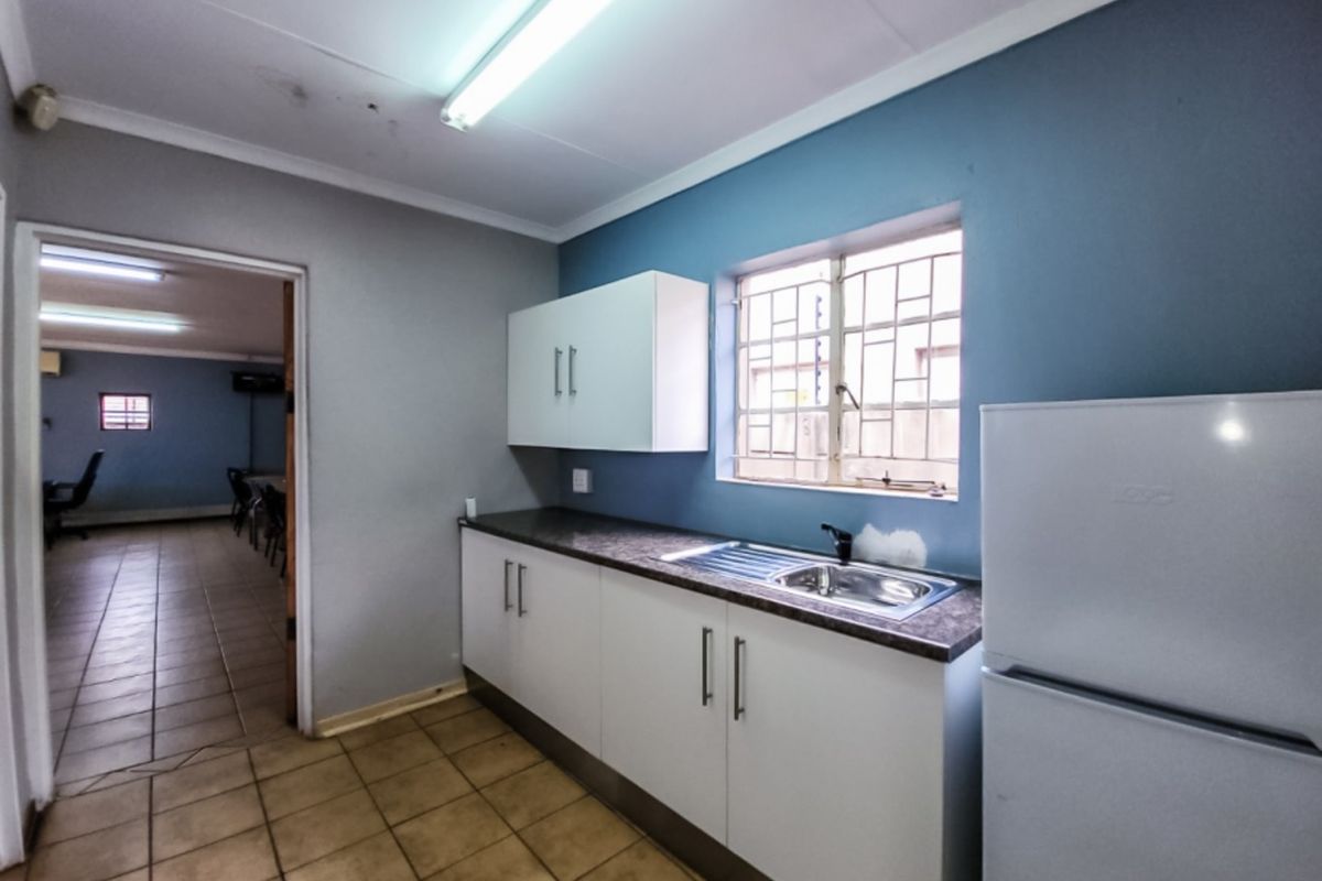 A functional kitchenette featuring white cabinetry, a stainless steel sink, and a window with security bars, providing a practical utility space.