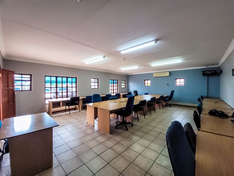 A spacious commercial office area featuring ceramic tile flooring, multiple windows for natural light, and a wall-mounted air conditioning unit.