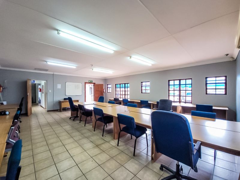 Spacious commercial office area featuring tiled flooring, multiple built-in desk stations, and ample natural light through grid-pane windows.