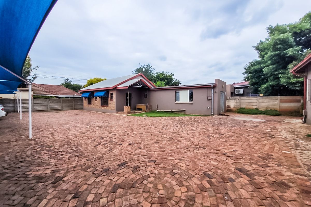 Rear exterior view of the commercial property featuring a large brick-paved courtyard, perimeter boundary walls, and a shade sail structure.
