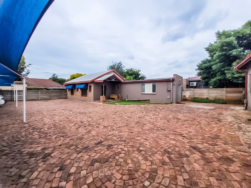 Rear exterior view of the commercial property featuring a large brick-paved courtyard, perimeter boundary walls, and a shade sail structure.