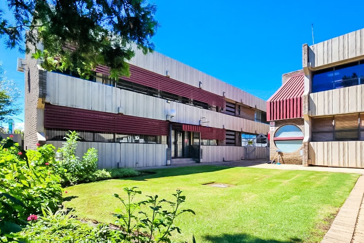 Rear view of a commercial building featuring a concrete facade, metal awnings, and a well-maintained lawn area with a paved walkway.