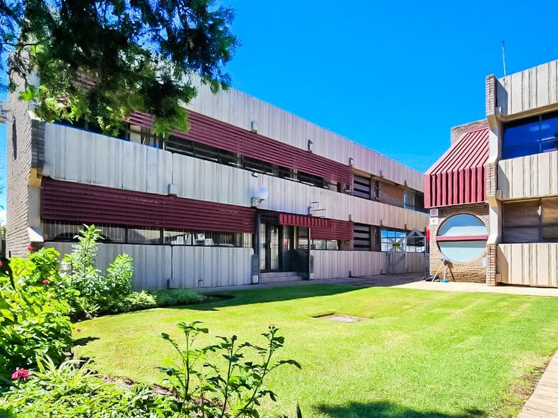 Rear view of a commercial building featuring a concrete facade, metal awnings, and a well-maintained lawn area with a paved walkway.