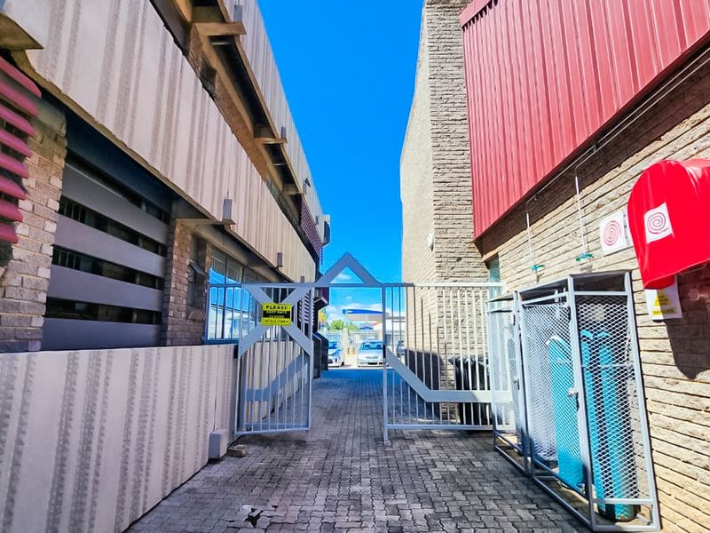 A secure rear service alleyway featuring brick paving, metal security gates, and dedicated storage areas for gas cylinders and fire safety equipment.