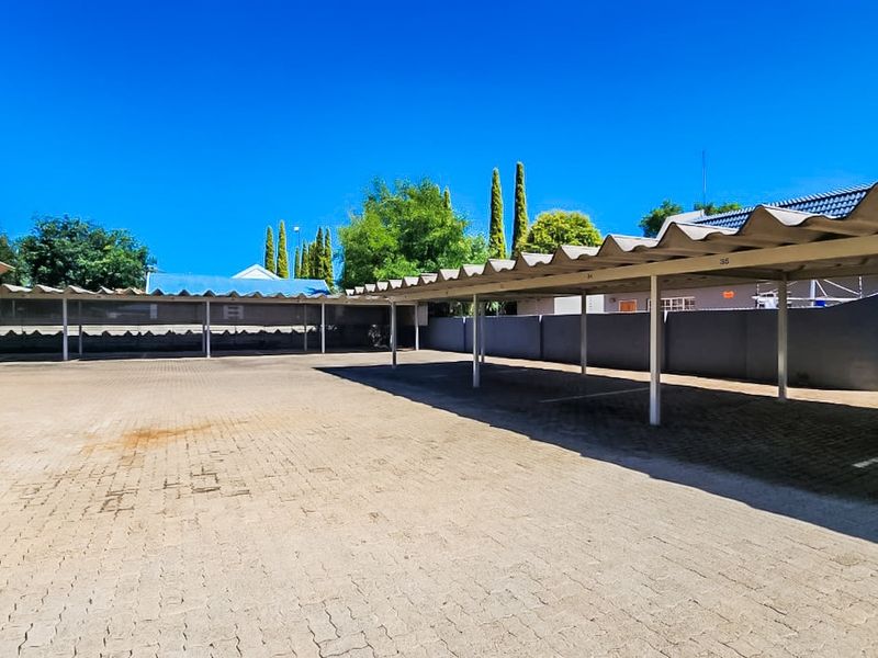 A spacious outdoor commercial parking area featuring multiple covered bays with paved surfacing and perimeter walling.