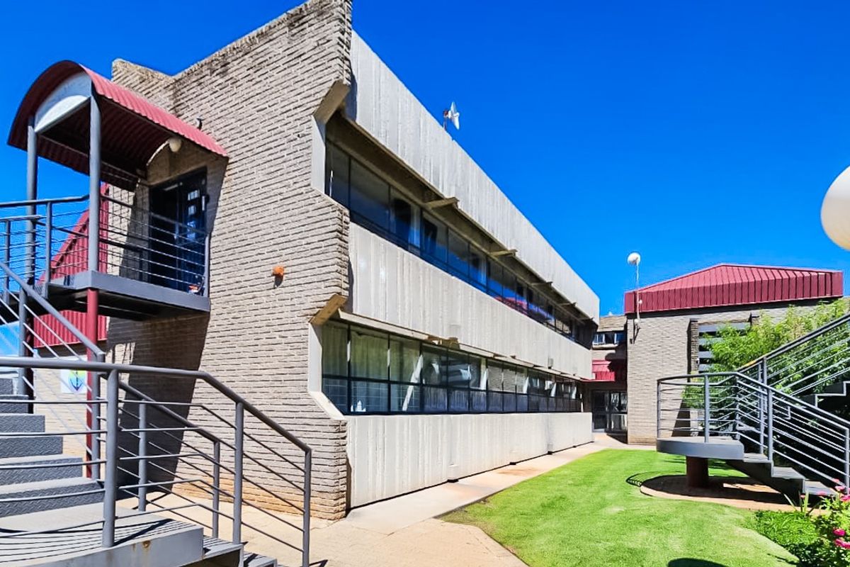 Exterior view of a commercial building featuring brick facade, metal staircases, and paved walkways with landscaped lawn area.