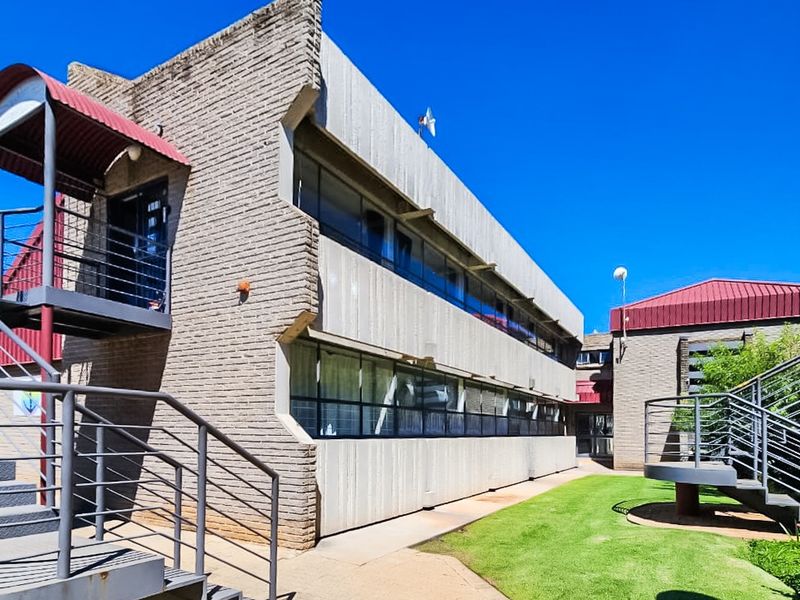 Exterior view of a commercial building featuring brick facade, metal staircases, and paved walkways with landscaped lawn area.