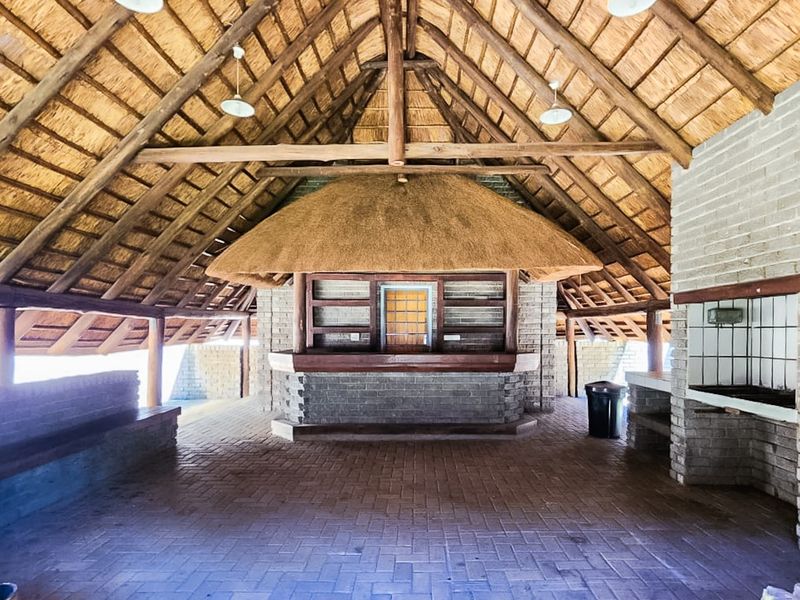 Spacious covered outdoor entertainment area featuring a traditional thatched roof, exposed timber trusses, a built-in brick bar, and a dedicated brick braai area.