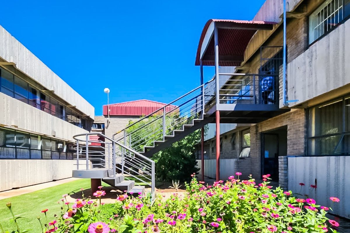 Exterior view of a commercial building complex featuring a central courtyard, landscaped garden, and an external metal staircase providing access to upper levels.