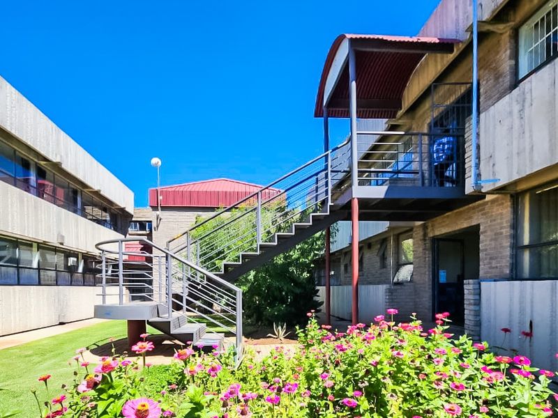 Exterior view of a commercial building complex featuring a central courtyard, landscaped garden, and an external metal staircase providing access to upper levels.