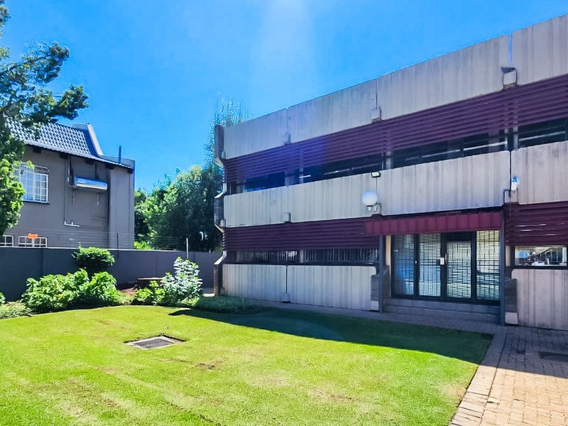 Rear view of a commercial building featuring a concrete facade with louvre shutters, a paved walkway, and a well-maintained lawn area.