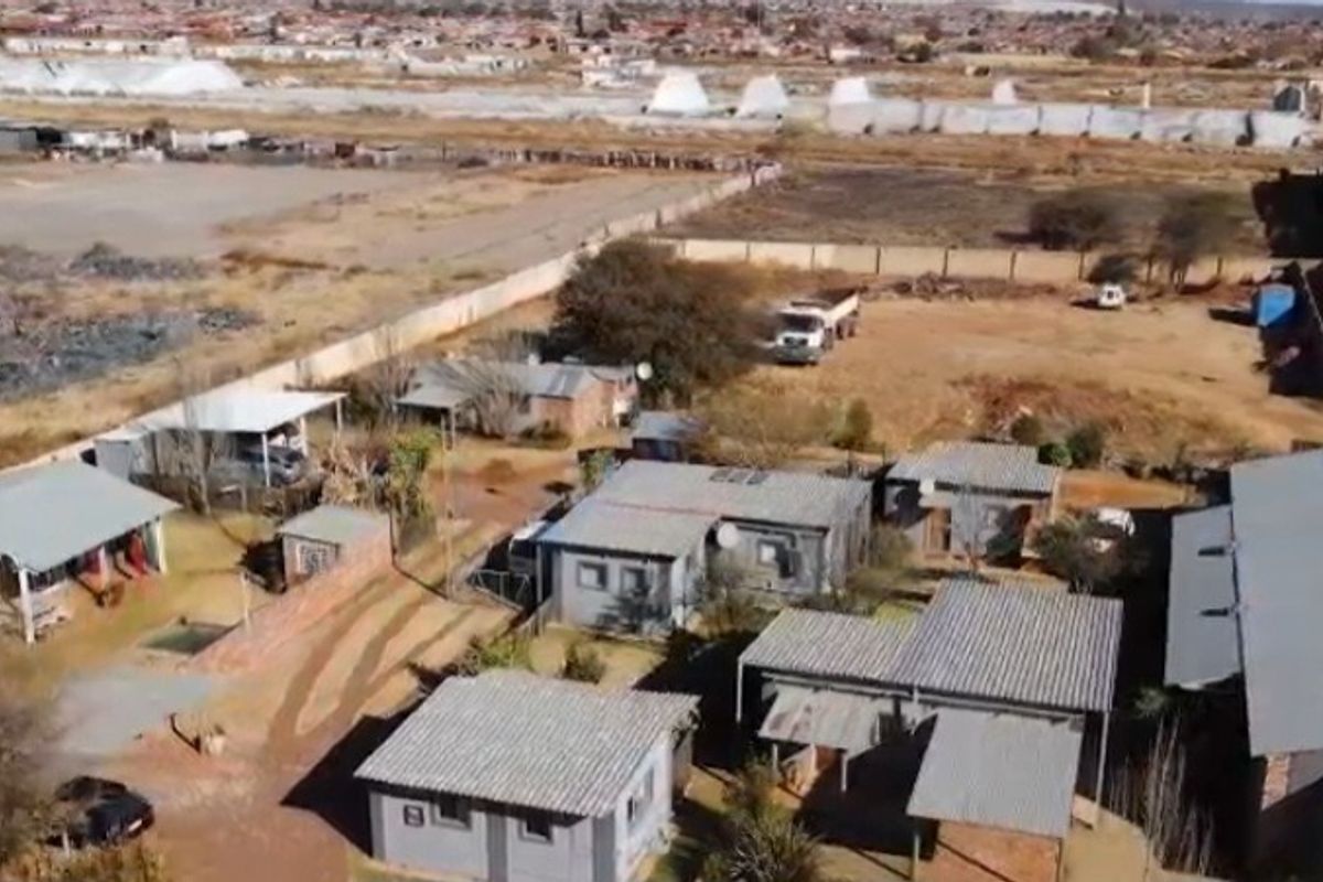 Aerial view of a business property featuring multiple detached structures with corrugated metal roofing, perimeter fencing, and paved access areas.