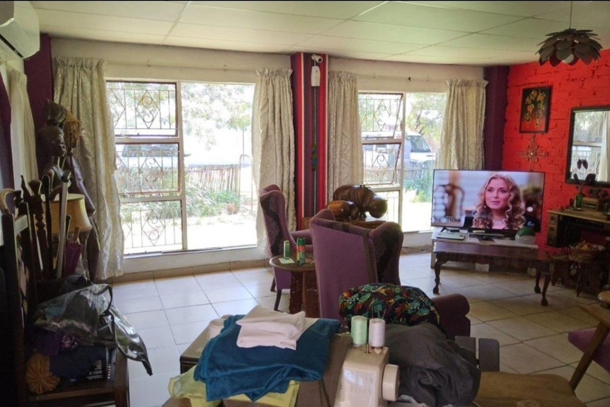 A living room featuring tiled flooring, security bars on windows, and an exposed brick feature wall, providing a functional but dated living space.