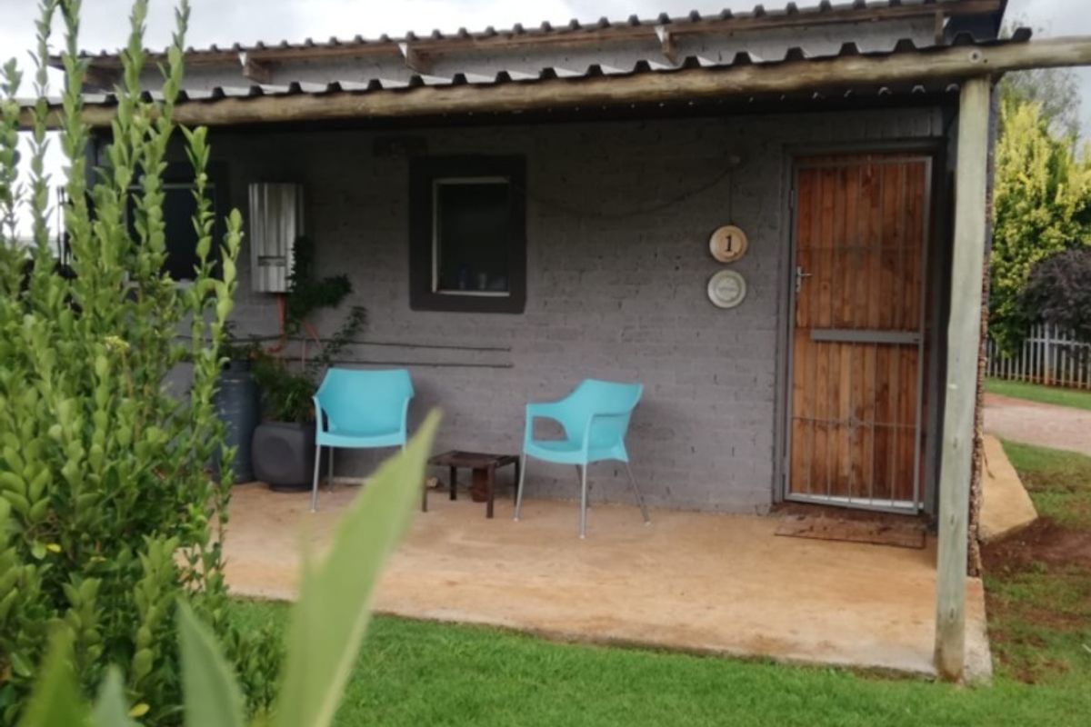A modest exterior view of a unit featuring a covered patio, timber entrance door, and external gas geyser installation set within a garden area.