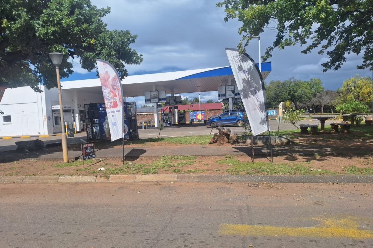 A commercial fuel station forecourt featuring a covered canopy, fuel pumps, and paved access area viewed from the street.