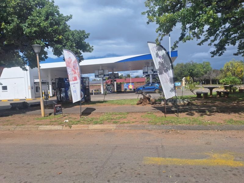 A commercial fuel station forecourt featuring a covered canopy, fuel pumps, and paved access area viewed from the street.