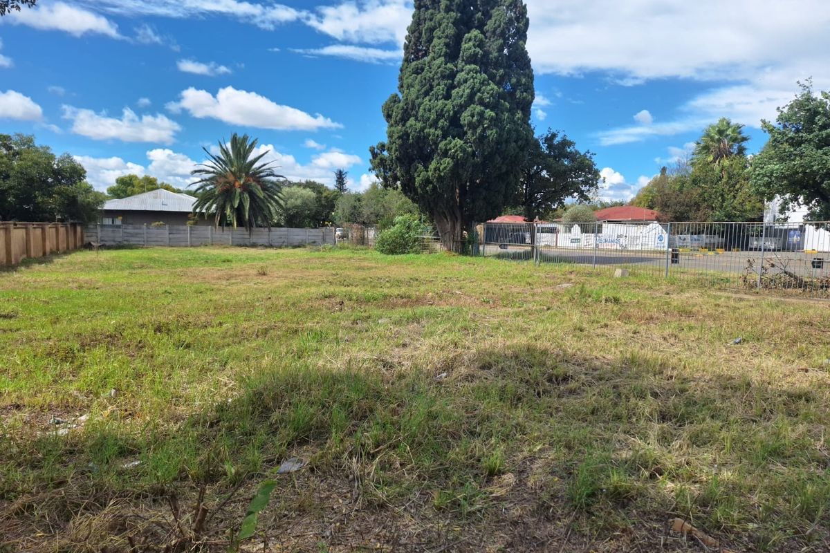 A vacant commercial land plot featuring established trees, grassed terrain, and perimeter fencing, offering a clear space for potential development.